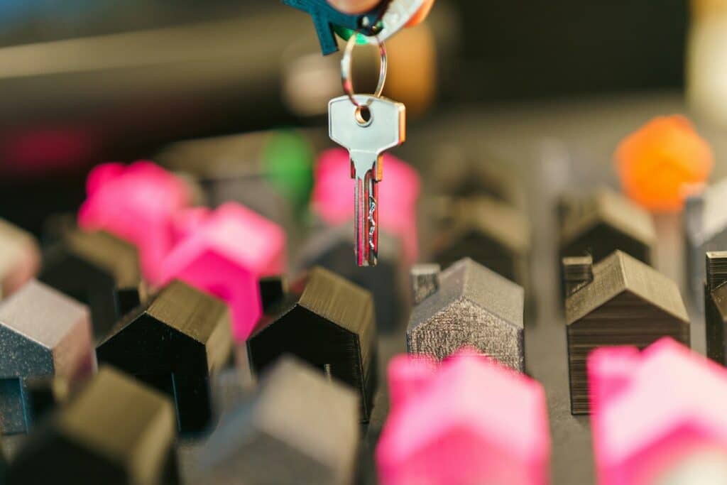 Hand holding a house key above miniature houses, comparing a cash offer to a listing