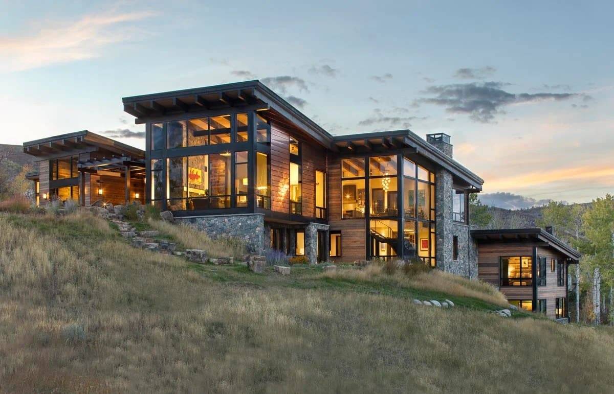 Mountain modern home of stone and glass on a hillside with aspens at sunset